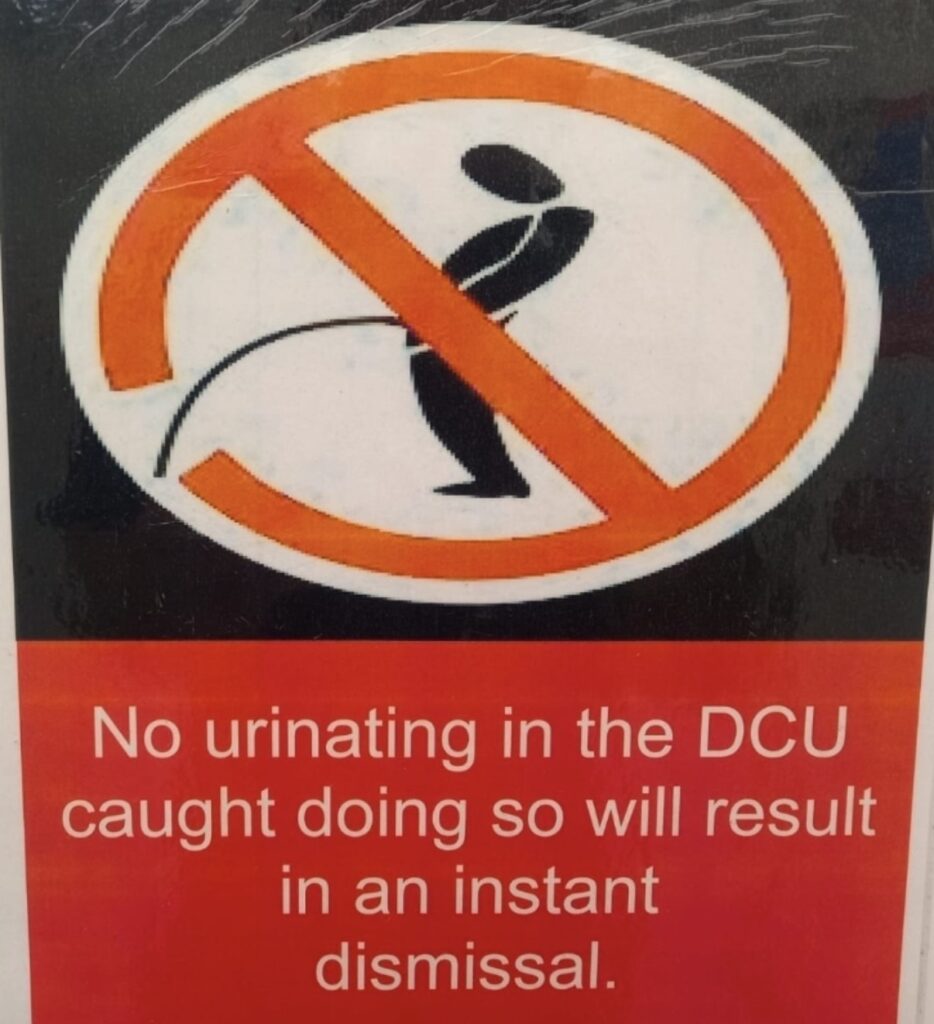 Safety sign inside a decontamination unit stating that urinating in the DCU will result in instant dismissal.