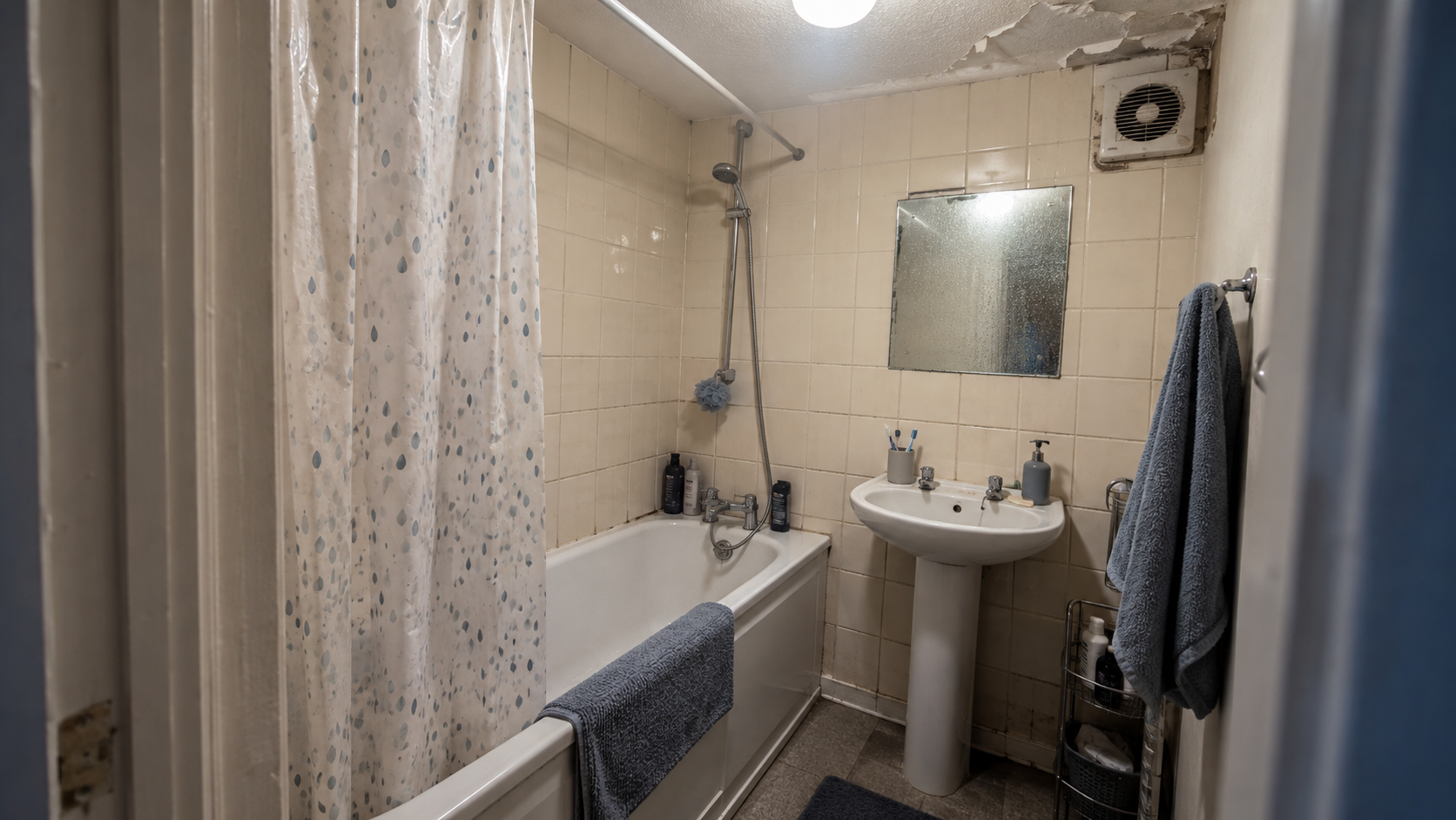A tired windowless British bathroom with peeling ceiling paint and a small extractor fan