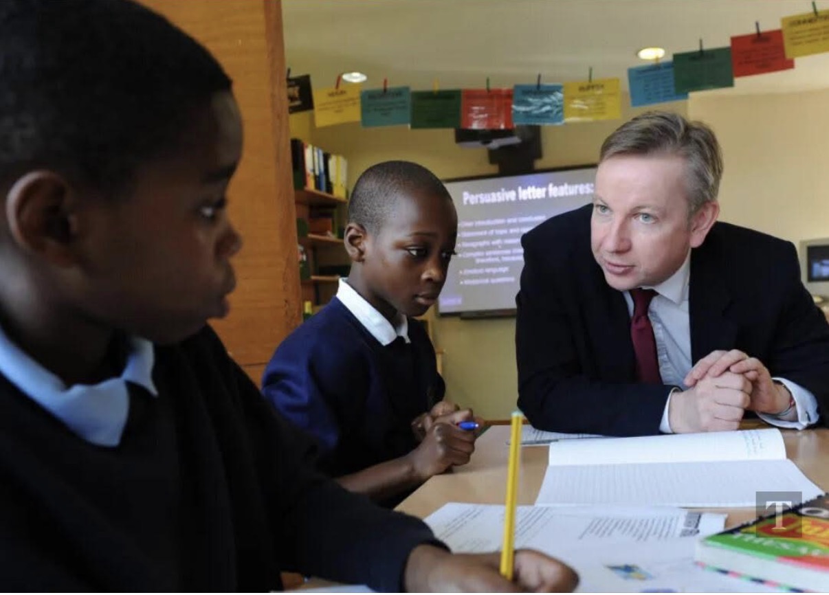 Michael Gove sitting at a classroom table with two Black primary-school pupils at Durand Academy in Stockwell in November 2010.
