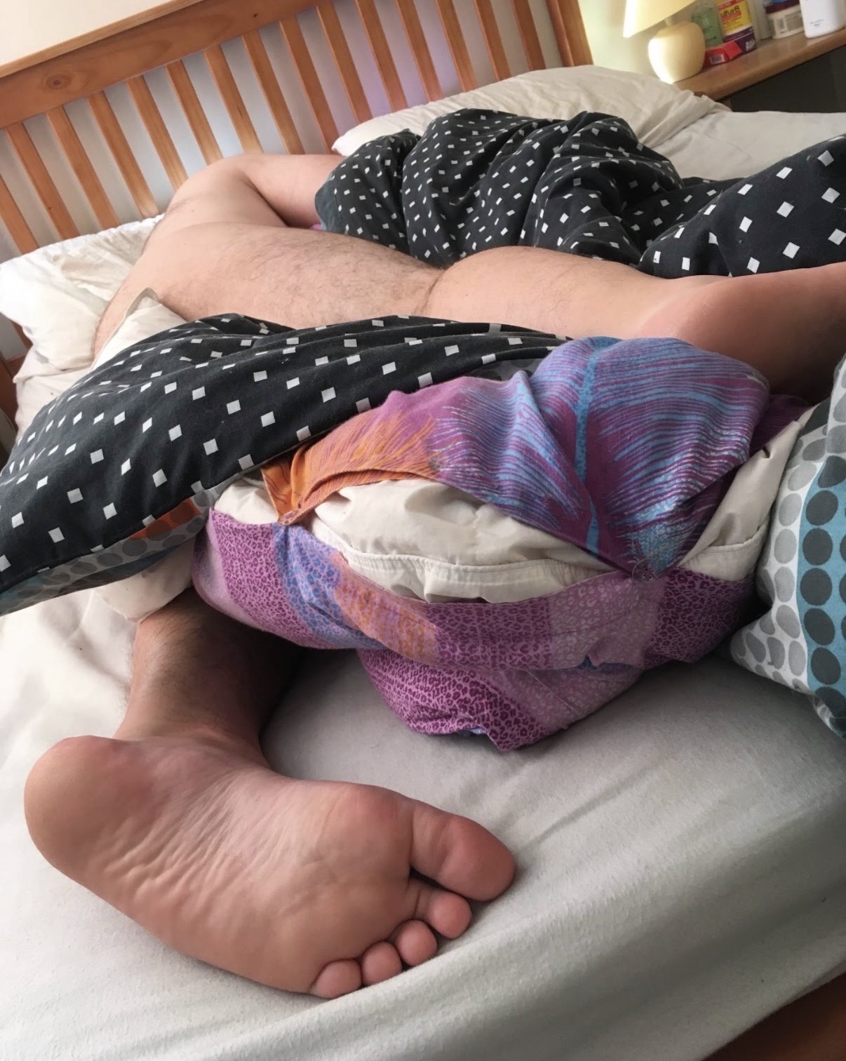 A man sleeping beneath patterned bedding with one bare sole resting close to the camera.